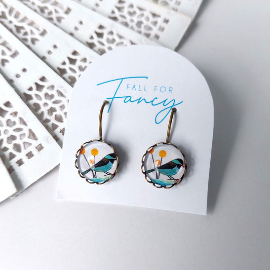 Glass dome earrings with filigree edge featuring a black and blue bird on a white background
